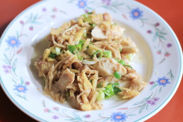 Ginger-fried chicken with sliced spring onions served on a white floral plate on an orange dining table.