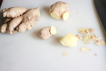 Ginger is being sliced on a plastic chopping board with a knife on an orange table.