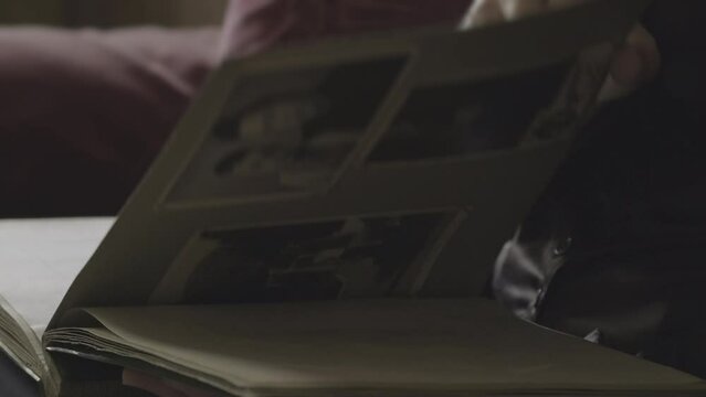 Human hand browsing old photo album pages. Woman is looking photo her family. Woman watching through retro photographs. Concept of biography nostalgia memories of youth, remembering relatives close-up
