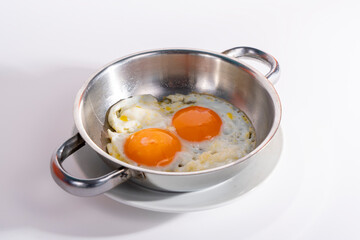 Cropped view of cracked double egg in pan, shot with selective focus from counter angle on white background in isolated setting.