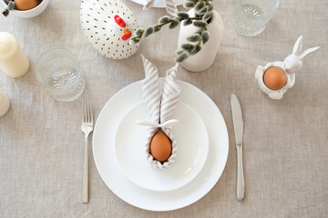 Easter setting table with Easter egg with rabbit ears made of napkin on plate.