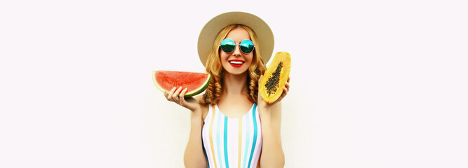 Obraz na płótnie Canvas Summer portrait of happy smiling young woman with slice of watermelon and papaya wearing straw hat, sunglasses, on white background