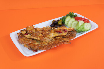 Cropped view of onion omelet with salad, olives and vegetables on white plate, shot in isolated area, orange background, with selective focus from opposite angle.