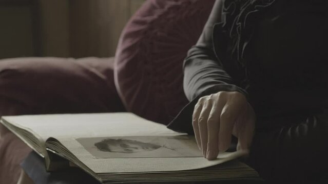 Human hand browsing old photo album pages. Woman is looking photo her family. Woman watching through retro photographs. Concept of biography nostalgia memories of youth, remembering relatives close-up