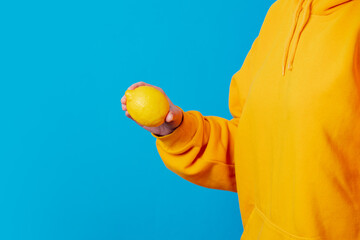 Stylish female in yellow hoodie with lemon on blue background