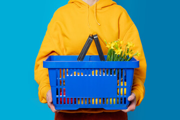Stylish female in yellow hoodie with blue basket and flowers on blue background