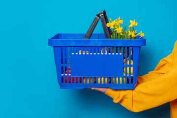 Stylish female in yellow hoodie with blue basket and flowers on blue background