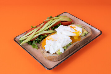 Cropped view of tomato and cucumber slices, greens and eggs on whole wheat bread on plate, shot with isolated area, orange background, with selective focus from opposite angle.