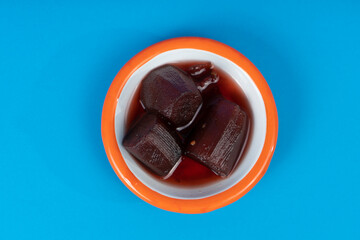 Cropped view of eggplant jam and white plate with orange rim shot with selective focus from overhead angle on blue background in isolated area.