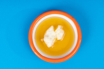 Cropped view of cream and cream with honey and white plate with orange rim shot with selective focus from overhead angle on blue background in isolated area.