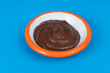 Close-up shot of black plate with hazelnut chocolate cream and orange rimmed in isolated area, blue background with selective focus from opposite or side angle.