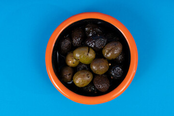 Cropped view of black plate with orange rimmed black and green olives with selective focus from overhead angle on blue background in isolated area.