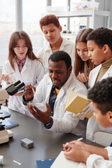 Vertical portrait of diverse group of children doing experiments with teacher in school chemistry...