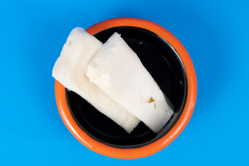 Cropped view of feta cheese slices and plate with orange rim shot with selective focus from overhead angle on blue background in isolated area.