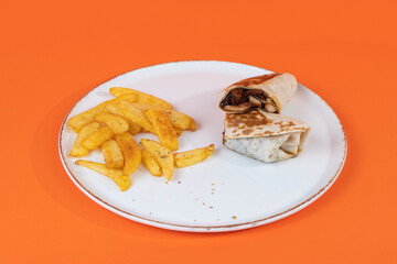 Cropped view of french fries and sliced chicken wrap on white plate shot with selective focus from opposite or side view on isolated orange background.
