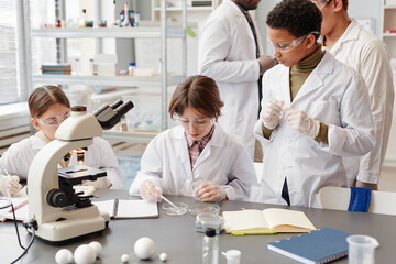 High angle view at diverse group of children enjoying experiments in chemistry lab at school, copy space