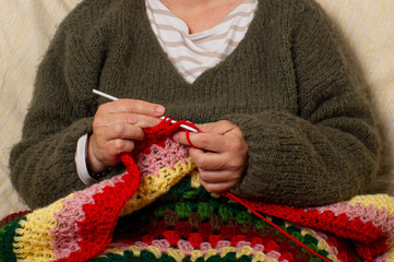 Manos mujer  tejiendo en crochet una manta de lana colorida