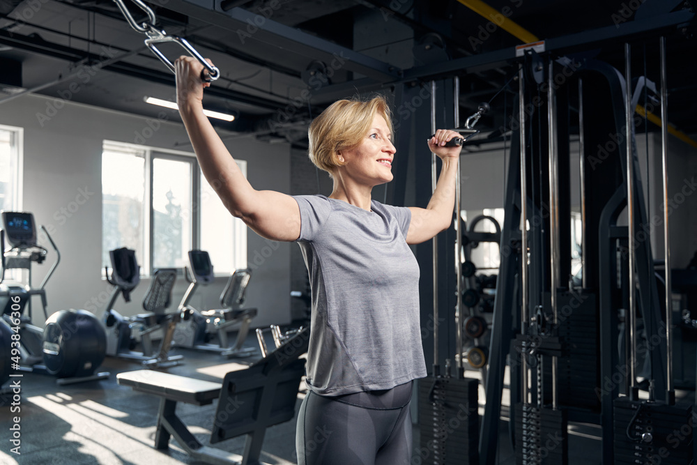 Wall mural Joyful woman using gym trainer in fitness center