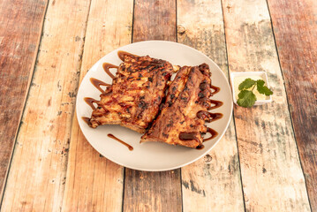 Delicious marinated and grilled pork ribs, served with barbecue sauce on a white plate, with sauce for dipping