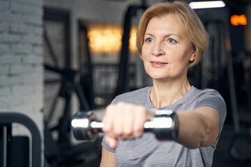 Naklejka na ściany i meble Woman doing exercise with dumbbell in fitness center
