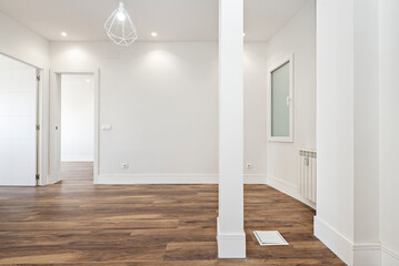 empty living room of a newly renovated apartment with open spaces, a matching column and the dining room with chestnut hardwood floors, white aluminum radiators