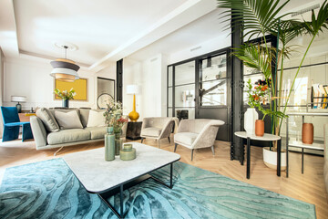 Living room with beautiful contemporary decor with wooden furniture, vases, chairs and armchairs, a large white potted palm tree and a black painted steel and glass wall