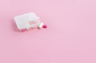 Pill box and tablets on pink background. Minimal concept of taking medications. Copy space, selective focus