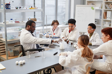 High angle view at African American teacher demonstrating science experiments to diverse group of...