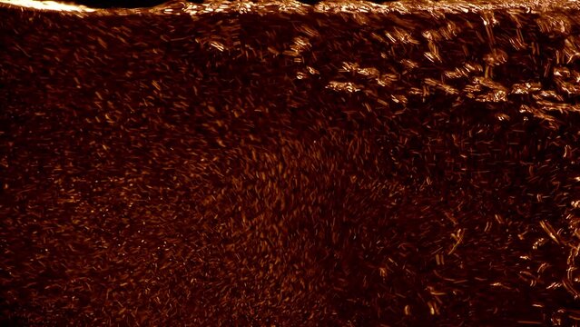 Dark home brew beer pouring into a glass. Extreme macro close-up of carbonated liquid beverage filling full screen on clean black background. Refreshing stream of a fresh drink.