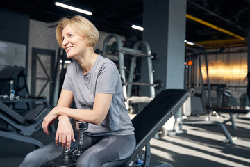 Fototapeta na wymiar Cheerful woman resting after workout in gym