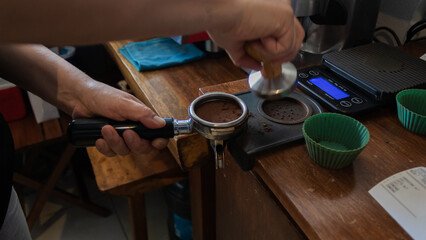 Fototapeta na wymiar Cropped view of barista in brown apron holding portafilter with ground coffee and tamper
