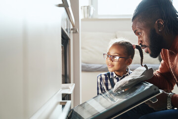 Little girl watching the cooking process in the oven with her father