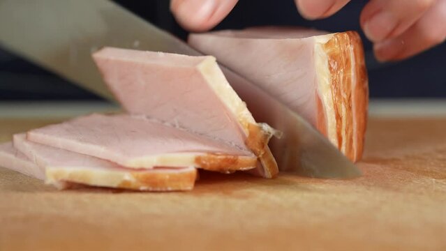 Slicing traditional ham into pieces on a cutting board with a knife. Thin slices of meat. home food