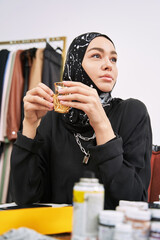 Young woman in hijab drinking tea in dress workshop
