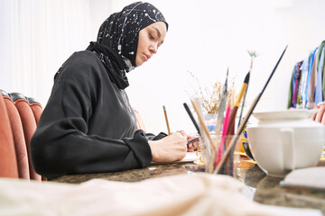 Muslim female designer creating clothes in sketchbook