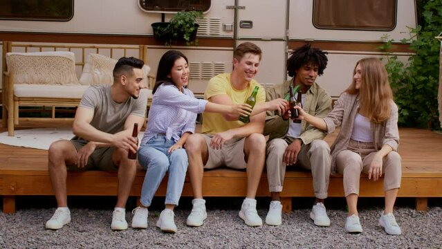 Cheerful Multiethnic Friends Sitting On Porch Near Trailer And Drinking Beer