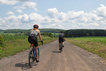 Fototapeta premium Vue de dos d'un couple de cyclistes faisant du vélo de gravelle sur une route tranquille dans la campagne par une journée d'été, ensoleillée.