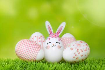 Easter eggs on the grass. Bunny egg and pink-decorated eggs against spring green bokeh background. Happy Easter composition.