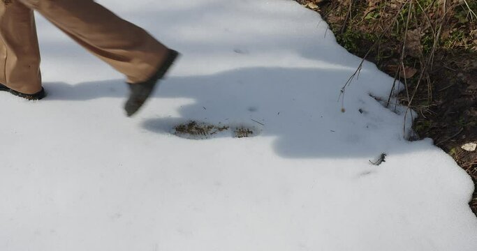 footsteps in the snow in black boots and light leather trousers. the legs of a girl in berets are walking in the snow, a shadow is silhouetted behind. close-up