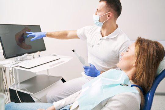 Male dentist showing results of dental 3D scanning to woman in clinic