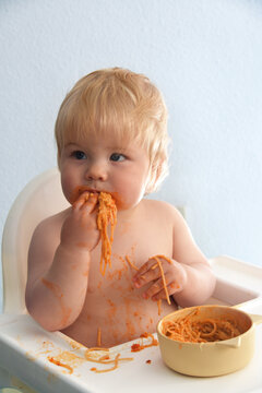Little baby boy eating spaghetti bolognese. Cute kid making a mess.