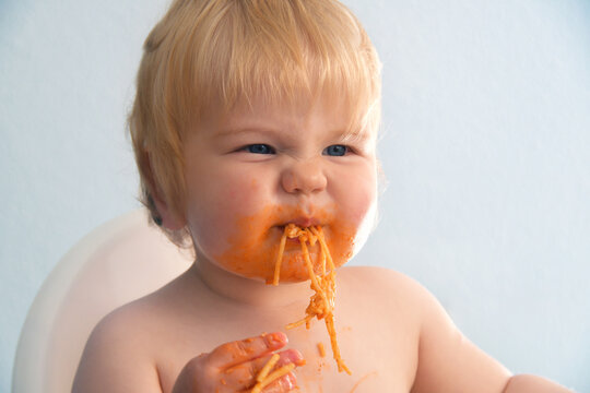 Little baby boy eating spaghetti bolognese. Cute kid making a mess.