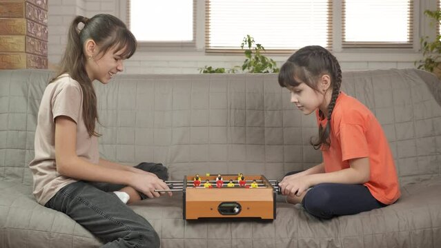 Friend time with foosball. Twi smiling cute friends play table soccer in the room.