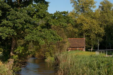 Small brown wooden hut on the bank of a small river in a cozy Bavarian village on a sunny day