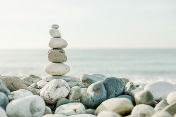 Fototapeta na wymiar Zen pyramid of balanced stones on a background of the sea and blue sky. Concept of spiritual harmony, balance and meditation. Peace and love in world