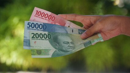 The Indonesian currency, the 20,000, 50,000 and 100,000 rupiah notes, are held in the hands of a...