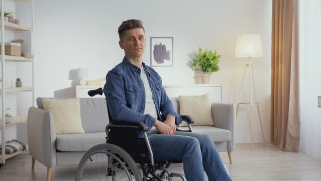 Calm mature man with spinal injury sitting in wheelchair and looking at camera, posing at home interior, tracking shot