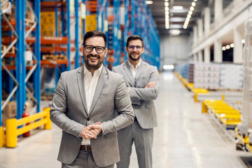 Two businessmen proudly standing and smiling at the camera in warehouse.