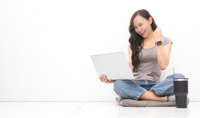 Fototapeta premium Beautiful Asian woman wearing grey casual shirt using laptop on white background and copy space. Cute Asian woman sitting on the floor room relaxing and excited something for work from home concept