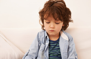 Its a no fun day. Shot of an unhappy-looking little boy sitting indoors.